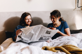 couple reading the newspaper and drinking coffee in bed after
              waking up refreshed