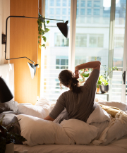 woman stretching
              in bed while looking out the window at the morning sun